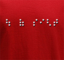 Red t-shirt background studded with Braille dots spelling "Out of Sight"